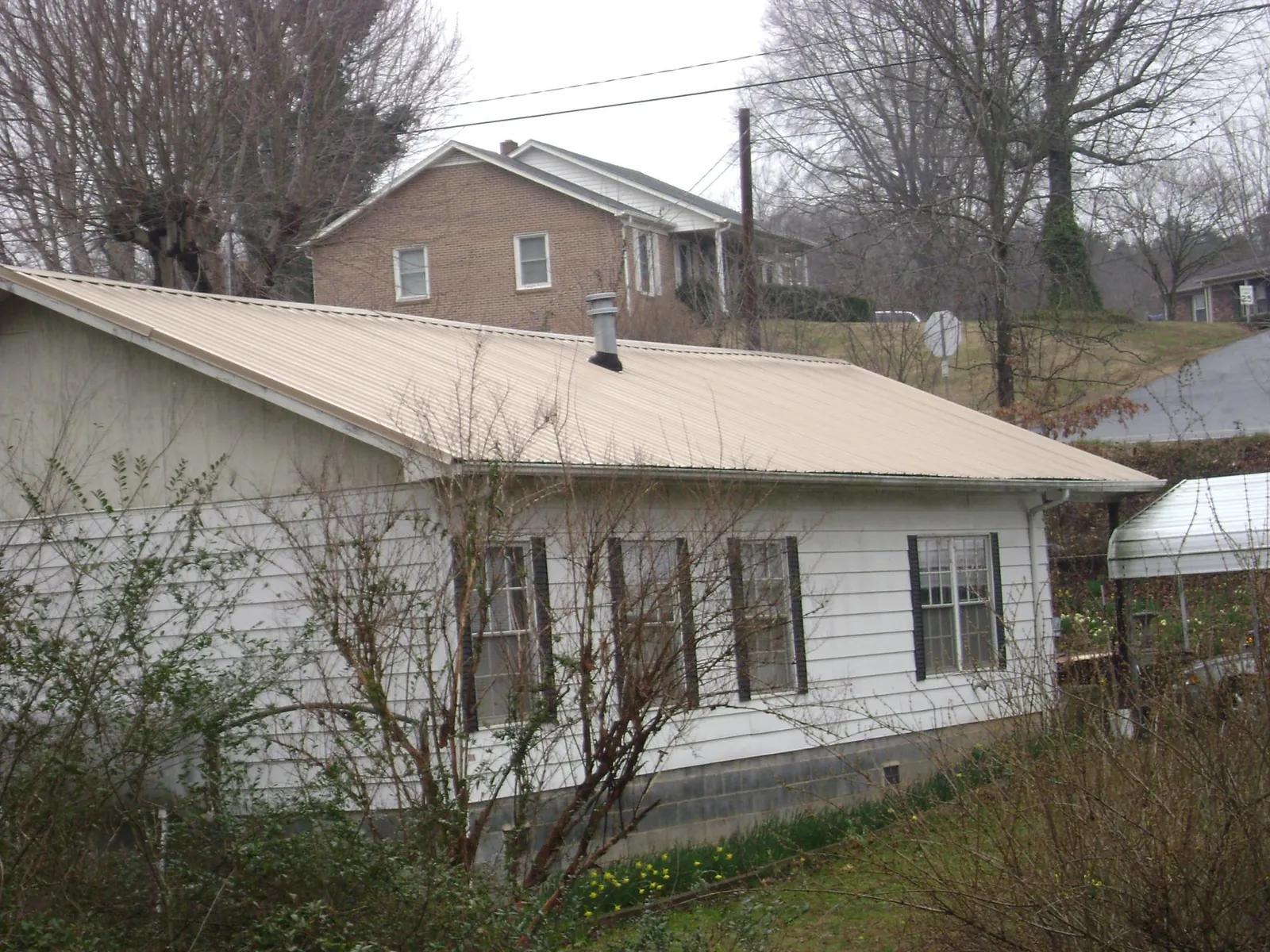 Tan metal roof on a white sided house set into a hillside — Commercial Roofing by Roofing Brothers in Saratoga